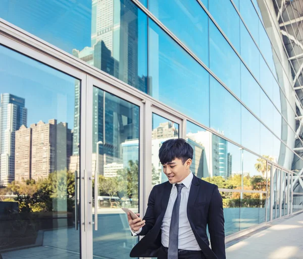 Hombre de negocios utilizando el teléfono móvil y de pie frente a offic —  Fotos de Stock