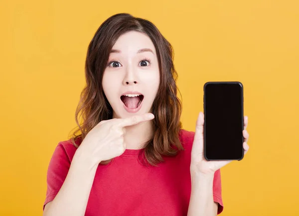 Здивована молода жінка показує смартфон — стокове фото