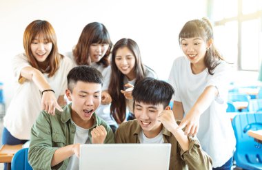 Sınıfta dizüstü bilgisayara bakan mutlu öğrenciler.