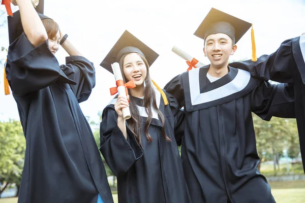 happy  students in graduation gowns holding diplomas on university campus