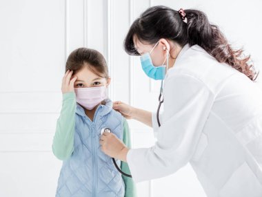 Doktor steteskoplu küçük kızı muayene ediyor.