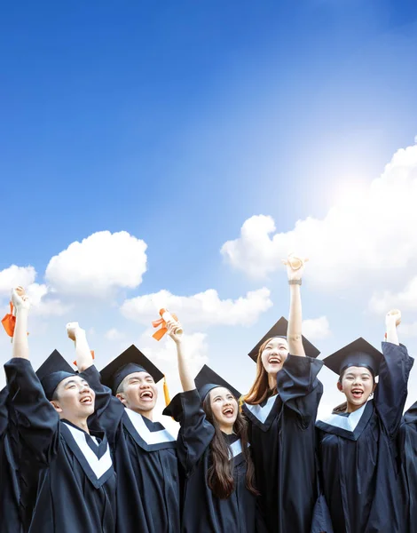 Szczęśliwi Studenci Sukniach Dyplomowych Posiadających Dyplomy Tle Chmur — Zdjęcie stockowe
