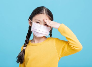 Tıbbi maskeli hasta kız çocuğu mavi arka planda izole edilmiş.