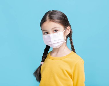 Tıbbi maskeli hasta kız çocuğu mavi arka planda izole edilmiş.