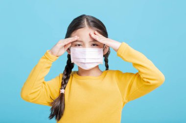 Tıbbi maskeli hasta kız çocuğu mavi arka planda izole edilmiş.