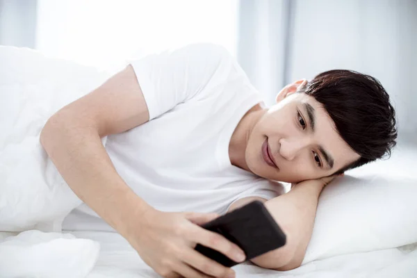 Knappe Jongeman Kijkt Naar Mobiele Telefoon Bed — Stockfoto