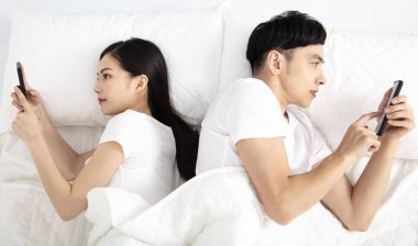 Yatakta akıllı telefonları olan genç çift