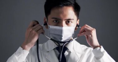 Asyalı genç doktor beyaz tıbbi ceket giyiyor ve steteskop tutuyor.
