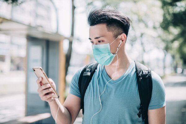 young man wear mask and walking on street using mobile phone