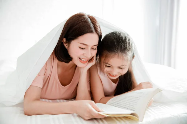 幸せな母親と娘読書本をベッドで一緒に — ストック写真