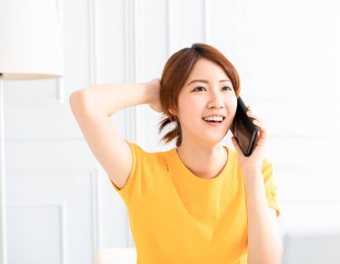 Gülümseyen genç bir kadın evde telefonla konuşuyor.