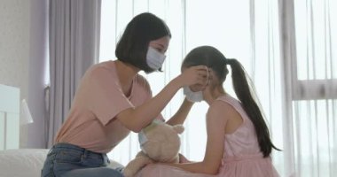 Anne kızına yatağında tıbbi maske takarak yardım ediyor.