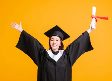 Mezuniyet elbiseli, diplomalı, başarılı bir jest yapan mutlu genç kadın.