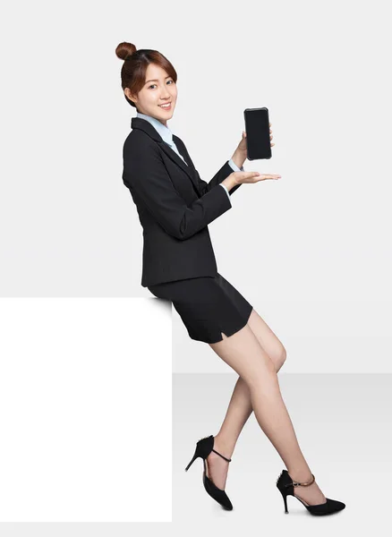 美しい若いビジネスマンの女性が白い看板に座ってスマートフォンを見せながら — ストック写真