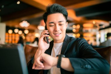 Kahve dükkanında dizüstü bilgisayar ve cep telefonuyla çalışan genç bir iş adamı.