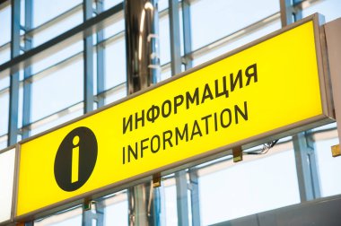 Uluslararası havaalanı, üstten sarkan siyah tahta, çeşitli bölgelere ve hizmetlere sarı yönlü işaretler.