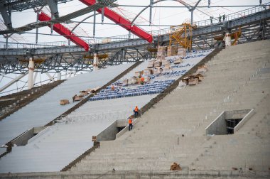 Stadyum inşaatı. Bir futbol stadyumunun inşaatı için inşaat malzemeleri ve işçiler. Koltuklar tribünde. Stadyumda çimensiz