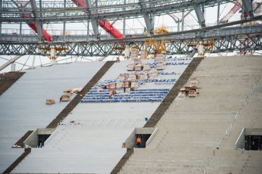 Stadyum inşaatı. Bir futbol stadyumunun inşaatı için inşaat malzemeleri ve işçiler. Koltuklar tribünde. Stadyumda çimensiz