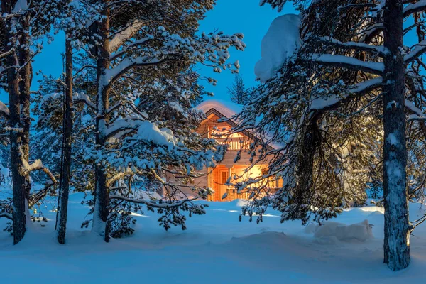 Casa din lemn cu lumină caldă în pădurea de iarnă rece întunecată — Fotografie, imagine de stoc