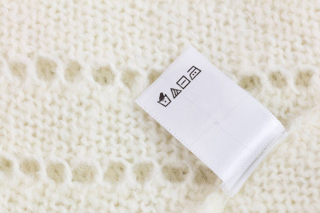 Laundry tag on white knitted wool sweater background