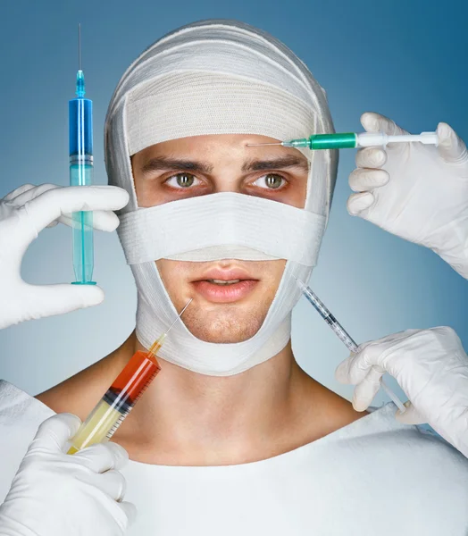 Man\'s face wrapped in bandages while many hands holding syringes near his face