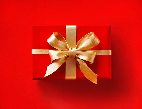 Gift box with golden ribbon on red background