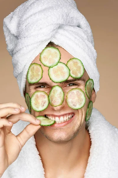 Funny man receiving facial mask of cucumber.