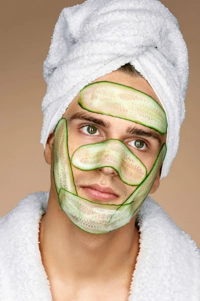 Fashionable man receiving facial mask of cucumber