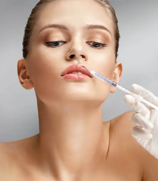 Beautiful woman face and beautician hands with syringe makes cosmetic injection in the upper lip. Clean Beauty concept