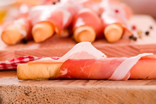 Grissini breadsticks with ham on wooden table. — Stock Photo, Image