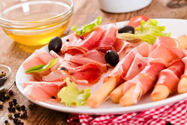 Grissini breadsticks with ham and olives. — Stock Photo, Image