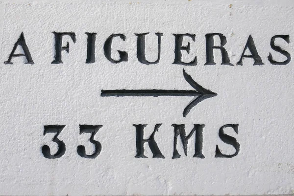 Roadsign on white wall with arrow pointing to Figueras at 33 km, — Stock Photo, Image