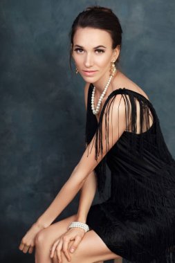 inci renk arka plan yanında oturan siyah elbiseli olan güzel zarif kadın portresi yarım uzunluk