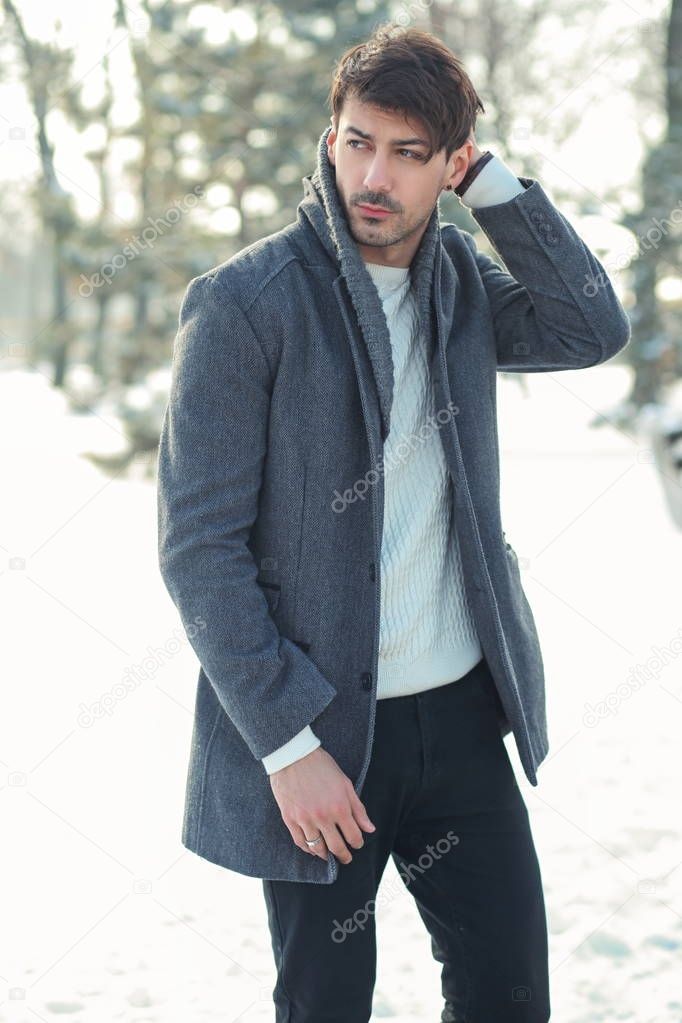 outdoor portrait of young handsome man in warm coat walking alone in snowy park