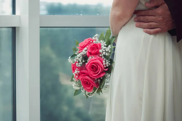 Νύφη σε ένα λευκό φόρεμα που αγκαλιάζει τον σύζυγό της, στεκόταν στο παράθυρο — Φωτογραφία Αρχείου