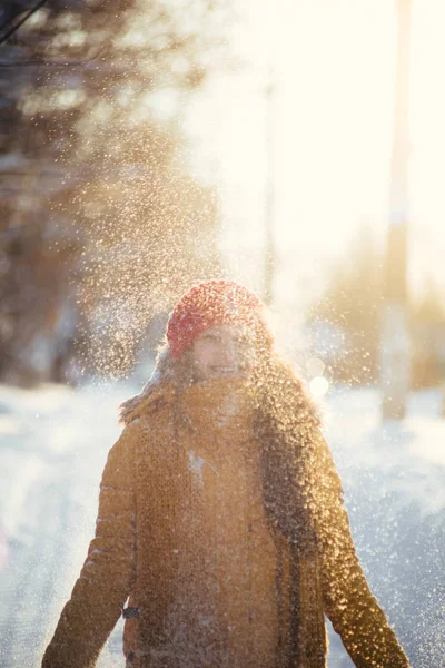 Charming girl in a yellow jacket and red cap throws snow in the air — Stock Photo, Image