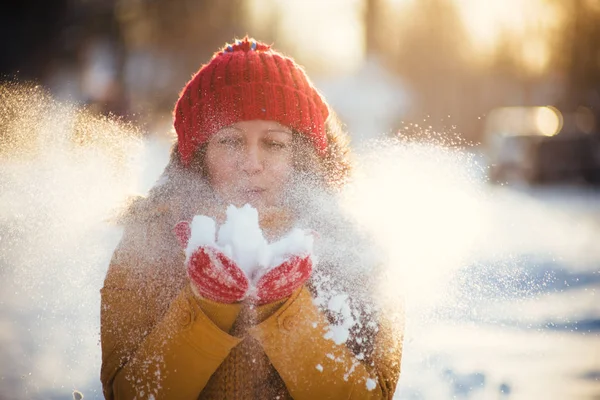 Charming girl in a yellow jacket and red cap throws snow in the air — Stock Photo, Image