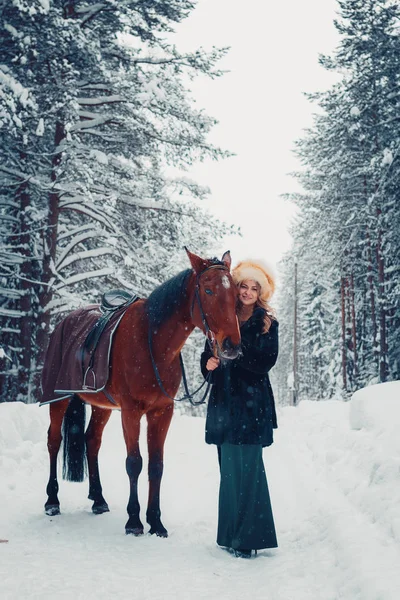 Foto van een mooi meisje in volle groei in zwarte jas, paard, winter — Stockfoto