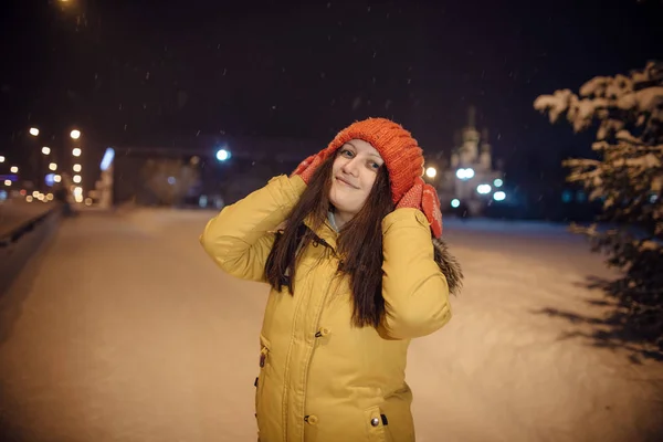 Girl's portret in de winter tijdens de sneeuwval, tegen de achtergrond van de kerk, een prachtige fir-tree en aantal lampen. — Stockfoto