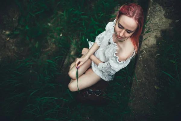 The beautiful girl with pink hair sits on the thrown ladder in an environment of a green grass — Stock Photo, Image