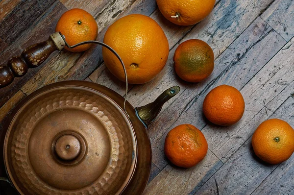 Vintage still life in dark colors. Iron kettle with oranges on scratched boards. — Stock Photo, Image