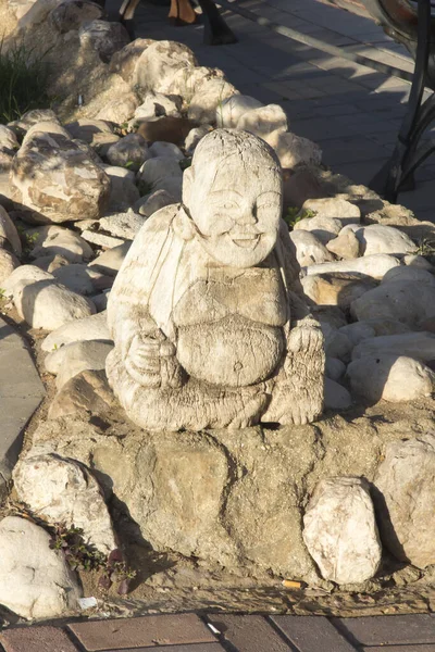 figurine of a small fat man in a sitting position as an element of small architecture at the sidewalk on the beach of the Dead Sea in Israel