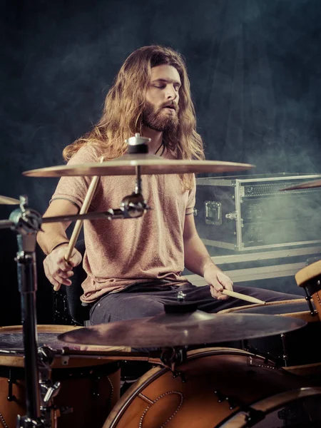 Молодой человек с длинными волосами играет на барабанах — стоковое фото