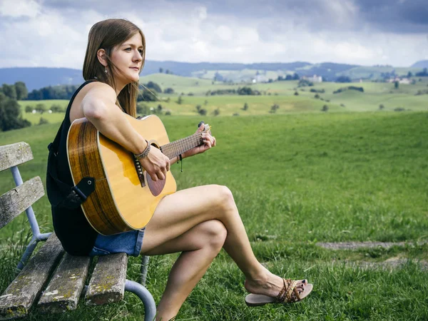 Woman playing guitar on a park bench — Stock Photo, Image