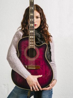 Akustik gitar tutan kızıl saçlı kadın.