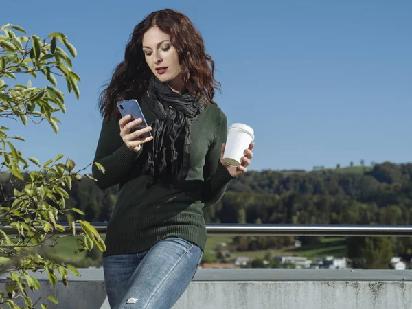 Frau checkt ihre Nachrichten und trinkt draußen Kaffee — Stockfoto