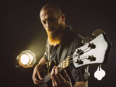 Spot ışığıyla bas gitar çalan sakallı adam.