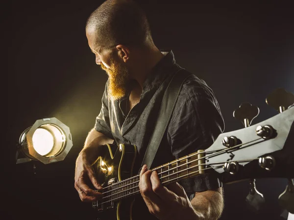 Spot ışığıyla bas gitar çalan sakallı adam.