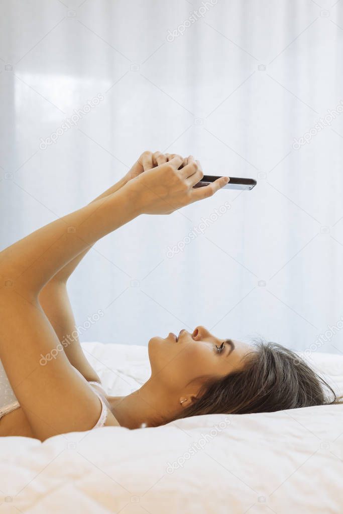 Sexy woman with smartphone lying on her bed