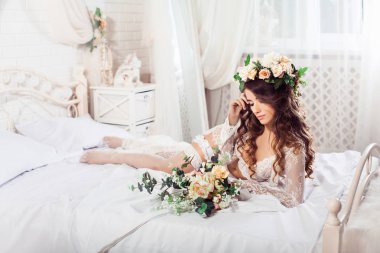 Seksi gelin buketi sabah bir yatakta yalan ile beyaz geceliği ve çelenk giymiş. Yatay. Serbest resim.